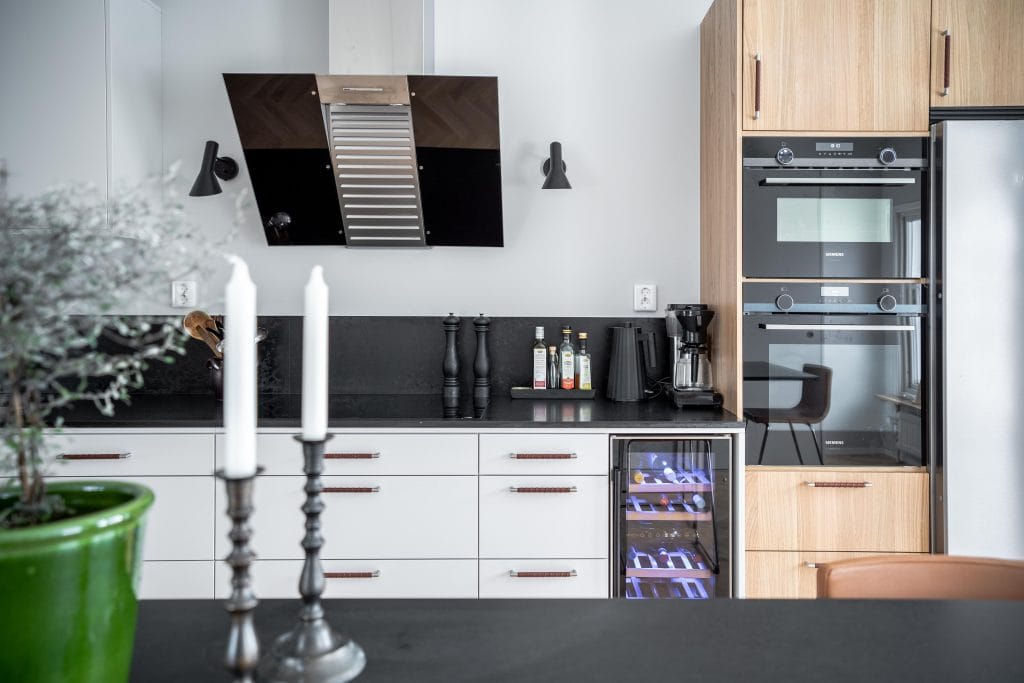 Kök med vita luckor, svart bänkskiva, vinkyl och ekskåp