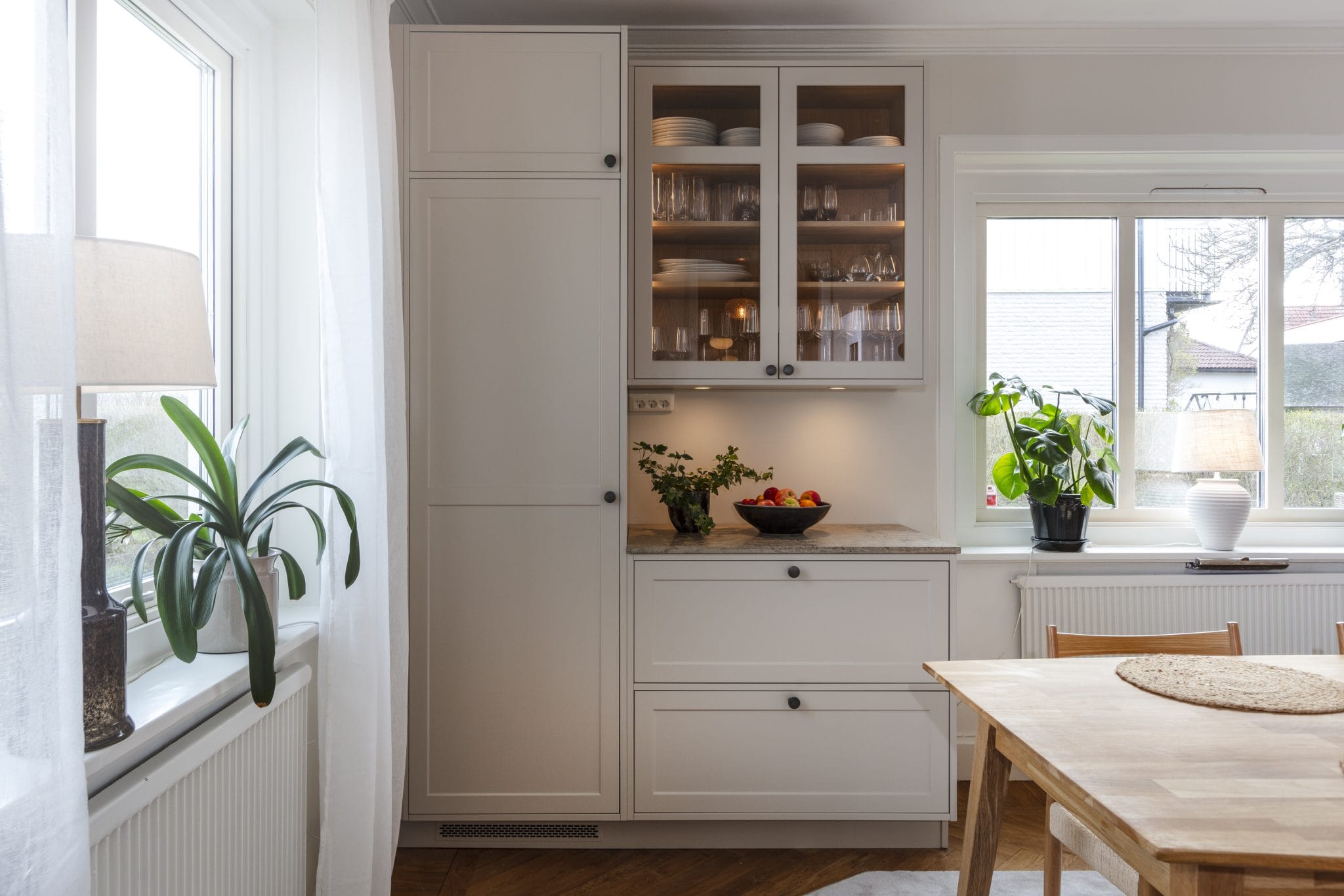 Vitt kök med vitrinskåp och matplats vid fönstret